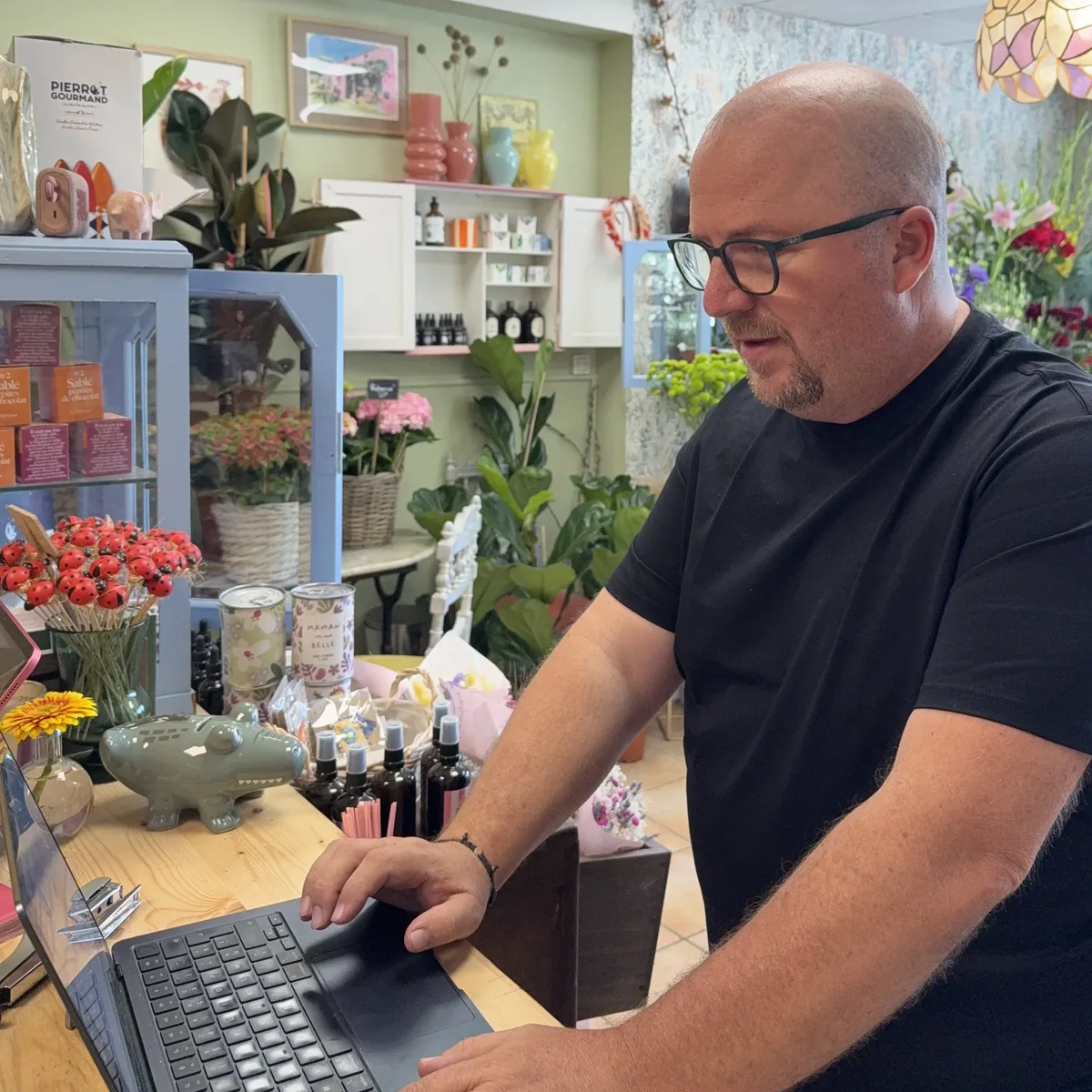 Mikaël travaillant sur ordinateur au comptoir de la boutique Rose Myrtille, entouré de fleurs